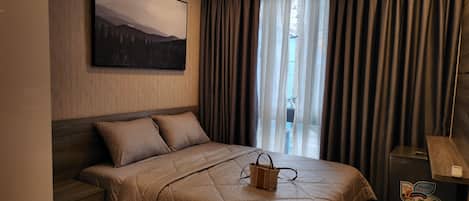 A hotel room with a bed, a nightstand, a dresser, a wall-mounted picture, and a window with curtains.
