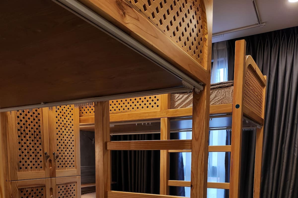 A bunk bed room with wooden bunk beds, a wardrobe, and a window with curtains.
