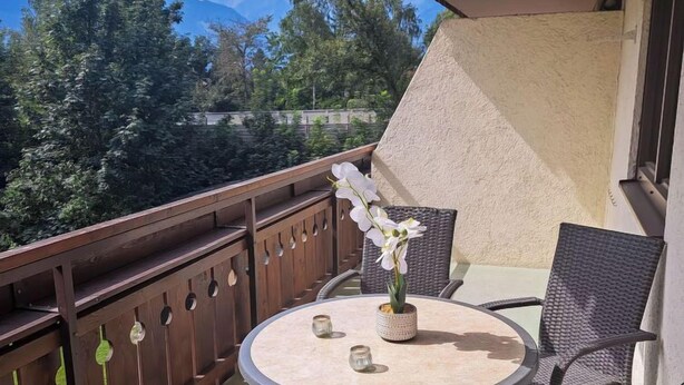 A balcony with a round table and wicker chairs, overlooking a mountainous landscape. - Kitzblick by Interhome (Zell am See)