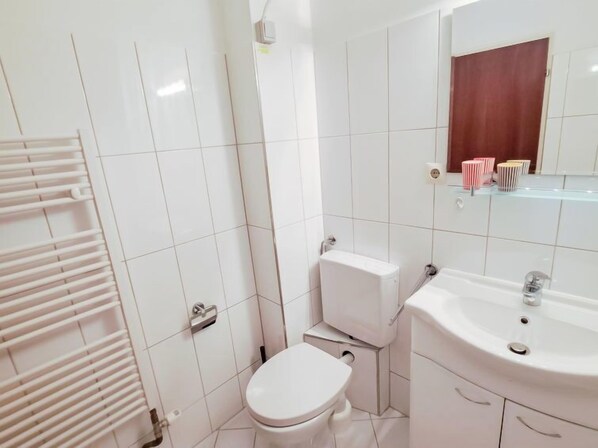 A bathroom with white tiles, a toilet, a sink, and a towel rack. - Kitzblick by Interhome (Zell am See)