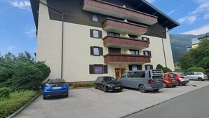 A multi-story building with balconies, a parking area, and a mountainous backdrop. - Kitzblick by Interhome (Zell am See)