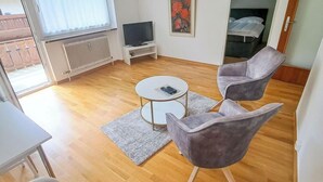 A modern living room with a round coffee table, two grey armchairs, a TV on a white stand, and a painting on the wall. - Kitzblick by Interhome (Zell am See)