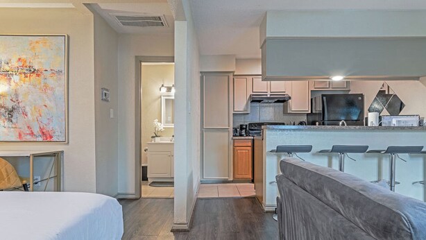 A modern hotel room with a large bed, a kitchenette, a dining area with bar stools, and a bathroom with a shower and toilet. - Your Montrose Estate! Sleeps 18/8BR/4BA/4PA<br> (Houston)