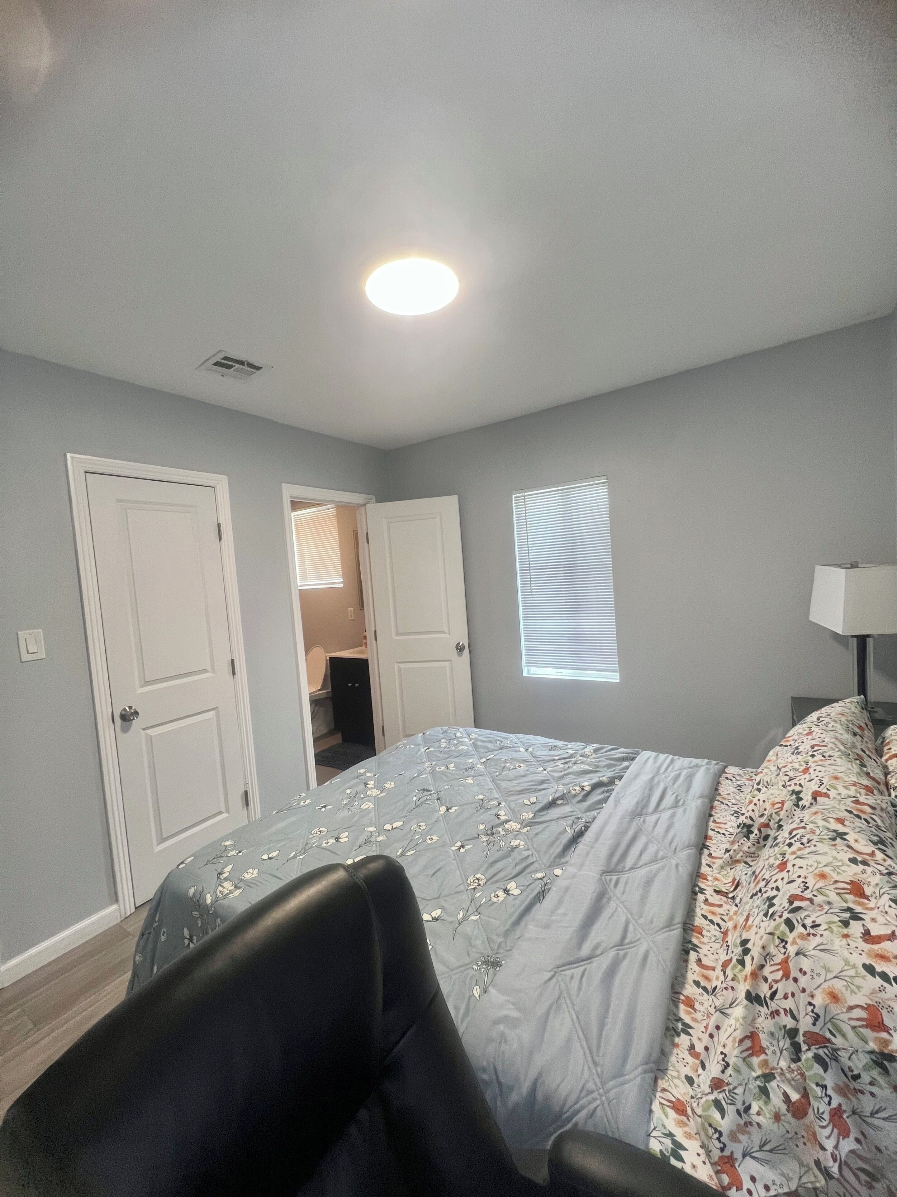 A bedroom with a bed, two doors, a window, and a nightstand with a lamp.