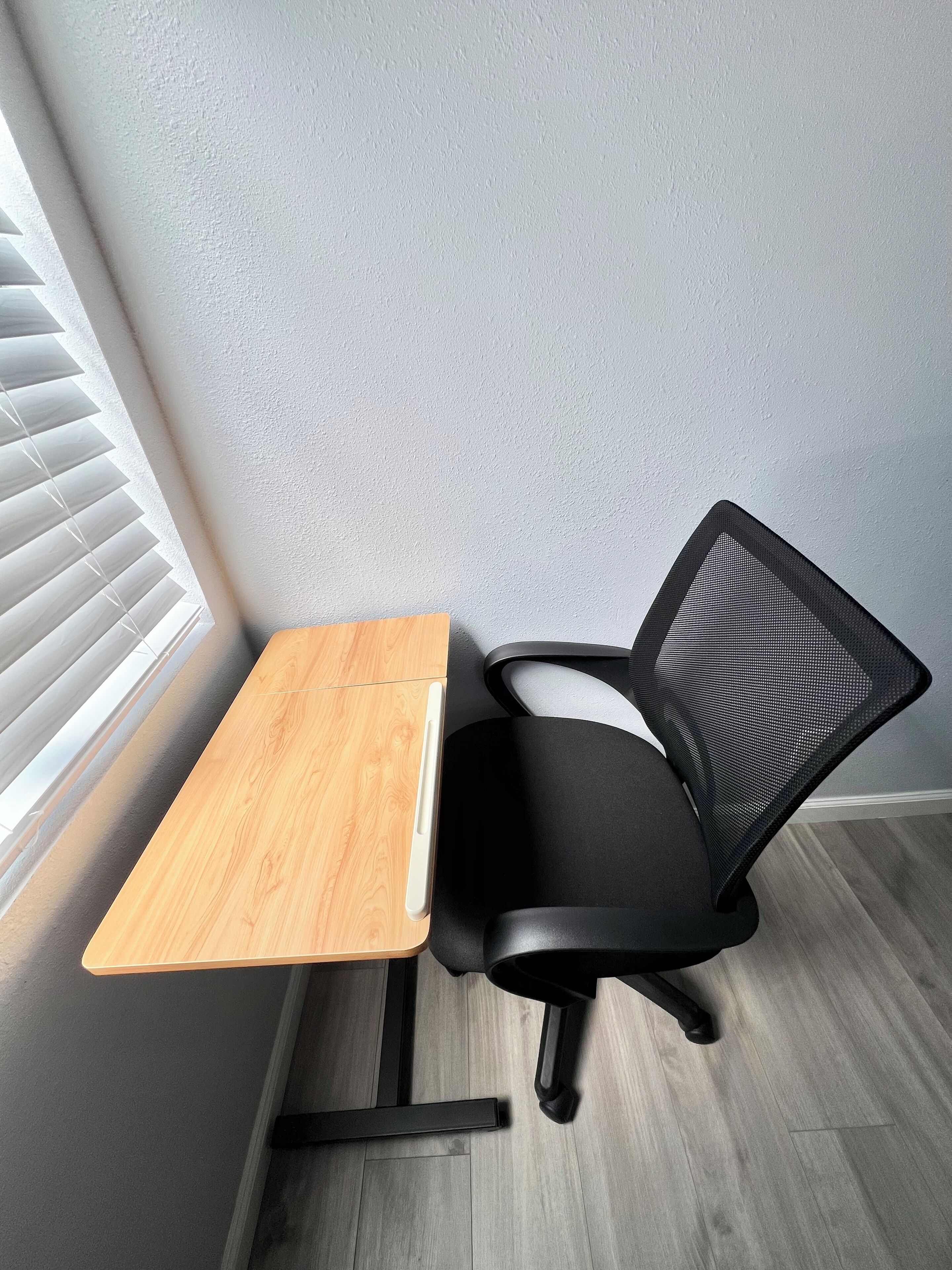 Een hoekbureau met een houten bureau en een zwarte bureaustoel.