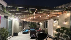 Une terrasse extérieure agrémentée de guirlandes lumineuses, d’un plafond en bois et de plantes en pot.