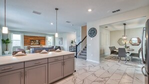A modern kitchen with a marble floor, a large island, and a dining area with a chandelier. - Chic Luxury Decor, Prime Location, Game Room Bliss (Kissimmee)