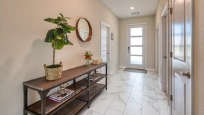 A hallway with a wooden console table, a potted plant, a mirror, and a door leading to another room. - Chic Luxury Decor, Prime Location, Game Room Bliss (Kissimmee)