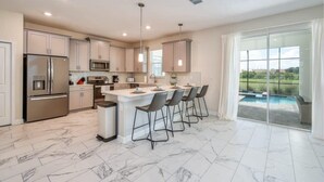 A modern kitchen with a central island, bar stools, a built-in oven, and a view of a swimming pool through large windows. - Chic Luxury Decor, Prime Location, Game Room Bliss (Kissimmee)