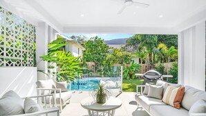 A modern outdoor living area with a pool, white furniture, and lush greenery. - The Santana Collection TWO - Luxury Villa Retreat in Palm Cove with Private Pool (Palm Cove)