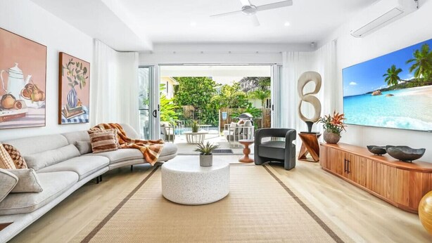 A spacious living room with a large TV, a sofa, a coffee table, and a view of a tropical beach through the glass door. - The Santana Collection TWO - Luxury Villa Retreat in Palm Cove with Private Pool (Palm Cove)