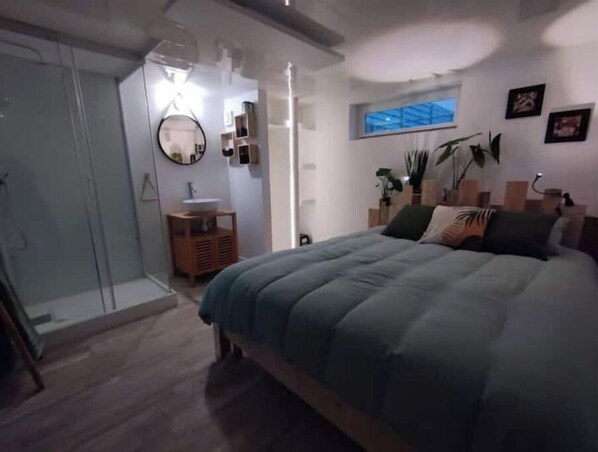 A modern bedroom with a large bed, a bedside table, a mirror, and a window.