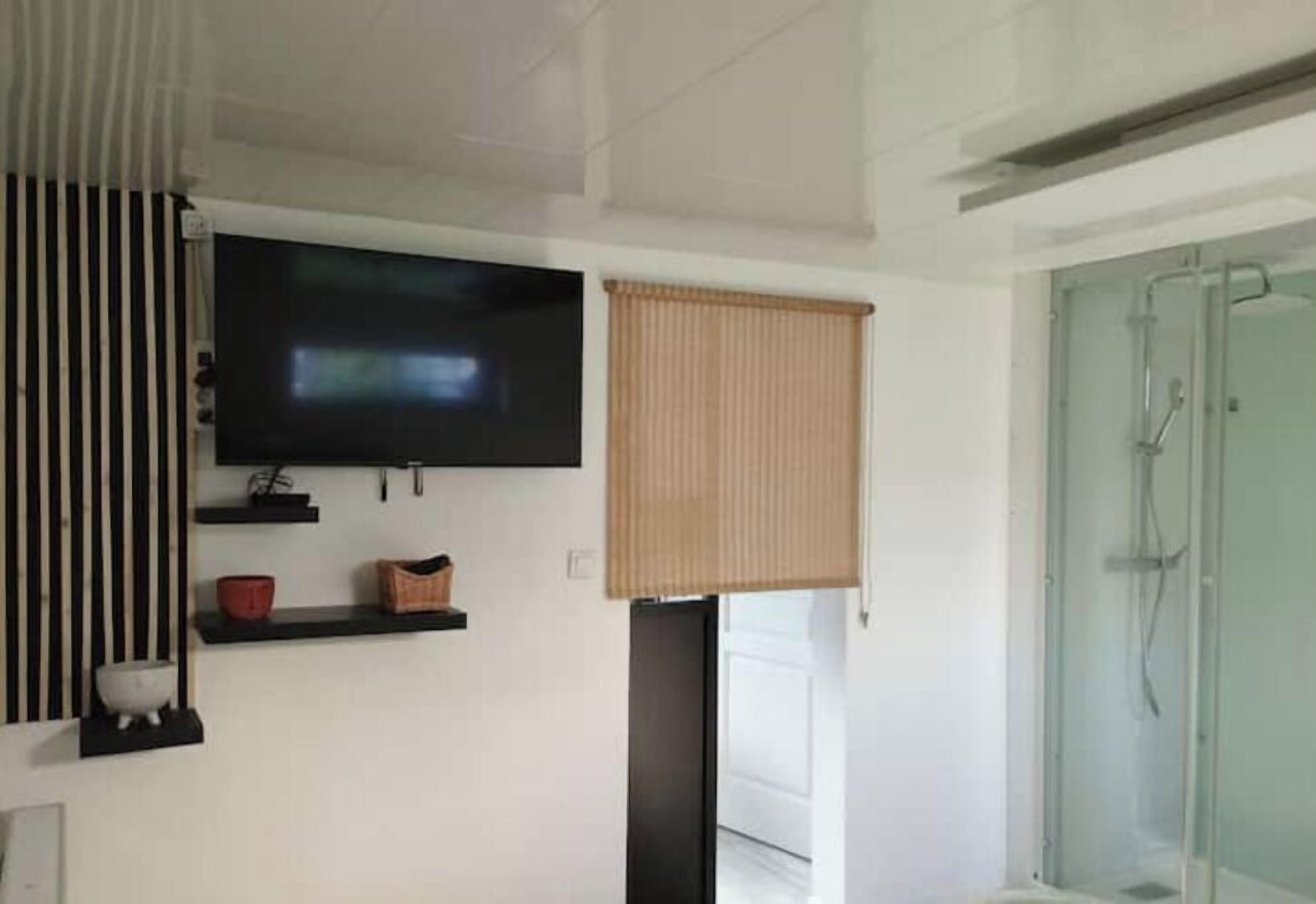Une salle de bain moderne avec une douche à parois de verre, un téléviseur fixé au mur et une étagère noire sur laquelle se trouvent une tasse rouge et un panier.