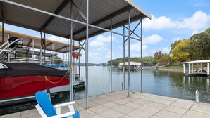 A dock with a covered seating area, a red boat, and a calm water body with boats in the background. - Blue Haven-Margaritaville-Private Dock and Kayaks! (Osage Beach)