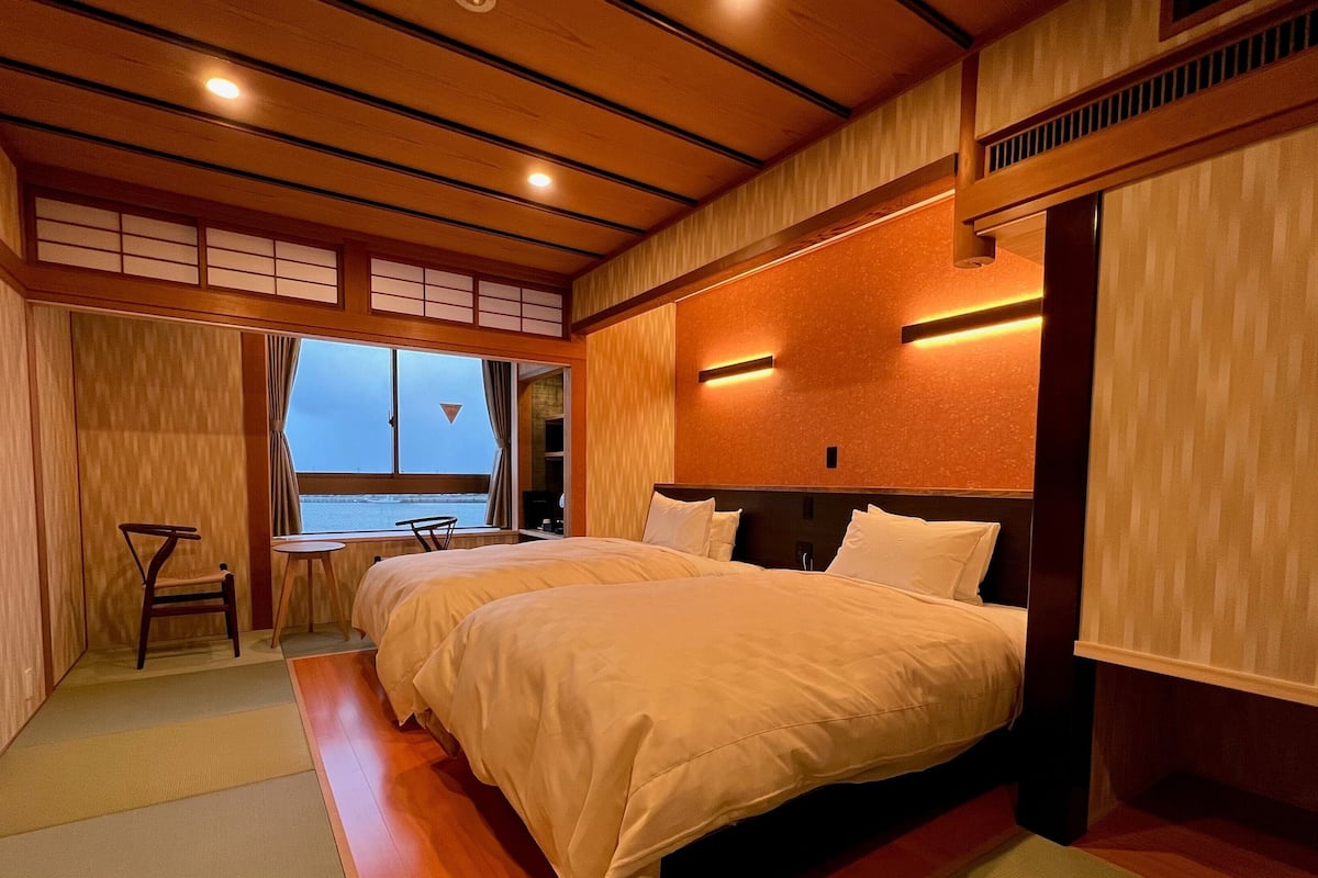 Une chambre d’hôtel avec un grand lit, une petite table et une vue sur la mer par la fenêtre.