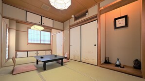 A traditional Japanese room with tatami flooring, a low table, a cushioned chair, sliding doors, and a shelf with decorative items. - Mikakunooyado Yamadaya (Tottori)