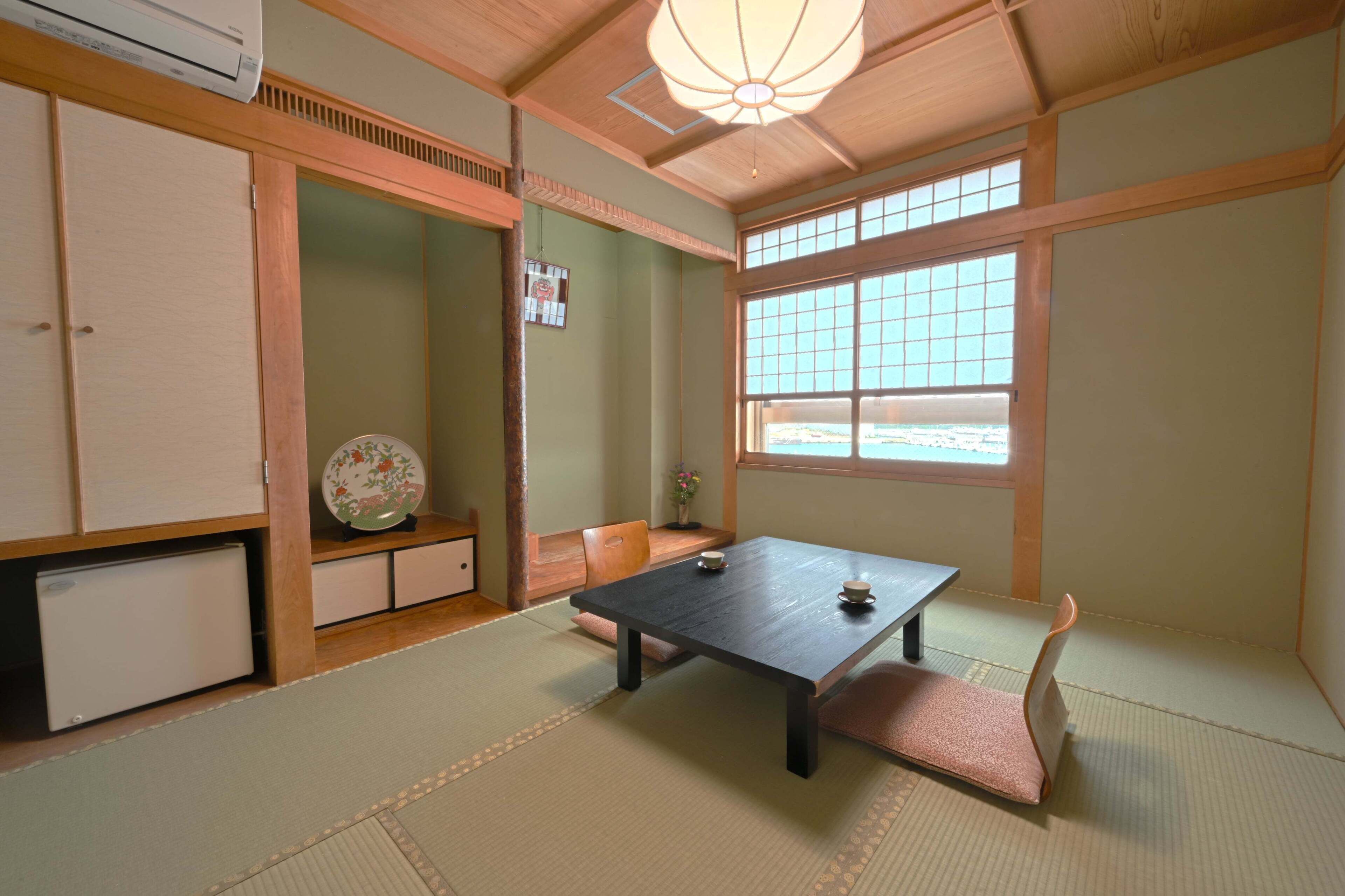 Ein traditioneller japanischer Raum mit Tatami-Böden, einem niedrigen Tisch, einer gepolsterten Sitzbank und einem Fenster mit Blick.