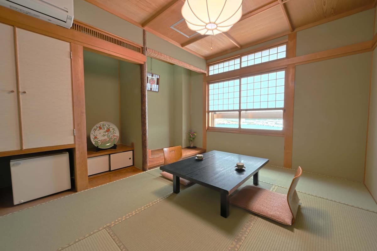 Une pièce de style japonais traditionnel, avec un sol recouvert de tatamis, une table basse, un banc rembourré et une fenêtre offrant une vue agréable.