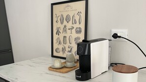 A kitchen counter with a coffee maker, a framed botanical print, and a white mug on a marble countertop.