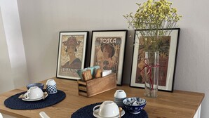 A dining table with a wooden top, white chairs, and blue placemats. There are framed pictures on the wall behind the table.