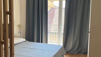 Une chambre avec un lit, une fenêtre avec des rideaux, un appareil de climatisation et une vue sur un bâtiment à l’extérieur.