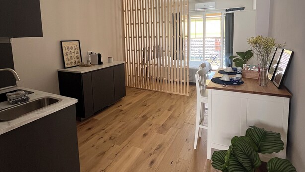 A modern kitchen with a wooden floor, a dining area with a white table, and a large green plant.
