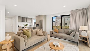 A modern living room with two sofas, a coffee table, and a kitchen in the background. - Wanaka Wonder - Wanaka Holiday Home (Wanaka)