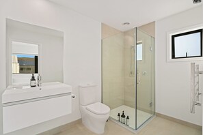 A modern bathroom with a glass-enclosed shower, a toilet, a sink with a mirror, and a window. - Wanaka Wonder - Wanaka Holiday Home (Wanaka)