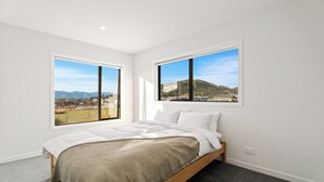 A bedroom with a bed, two windows with views of a landscape, and a carpeted floor. - Wanaka Wonder - Wanaka Holiday Home (Wanaka)