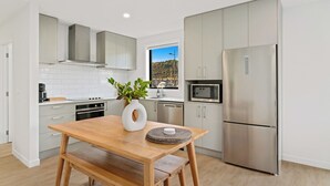 A modern kitchen with white cabinets, a stainless steel refrigerator, and a wooden table with a vase and placemats. - Wanaka Wonder - Wanaka Holiday Home (Wanaka)