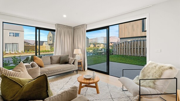 A spacious living room with a large sliding glass door leading to a backyard, a sofa set, a coffee table, and a chair. - Wanaka Wonder - Wanaka Holiday Home (Wanaka)
