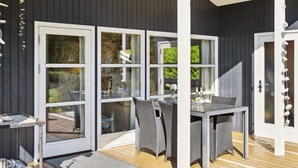 A covered outdoor dining area with a table and chairs, large sliding glass doors, and a wooden deck.