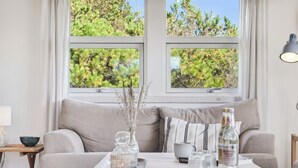 A cozy living room with a sofa, a coffee table with decorative items, and large windows with a view of trees.