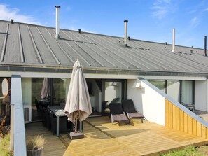 Moderni rakennus, jossa on kalteva katto, ulkona oleva oleskelualue ja suuret ikkunat.