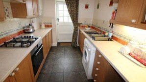 A compact kitchen with wooden cabinets, a gas stove, a washing machine, and a sink. - Rose Cottage: Romantic Dog‑Friendly Cottage with peaceful views & private garden (Cramlington)