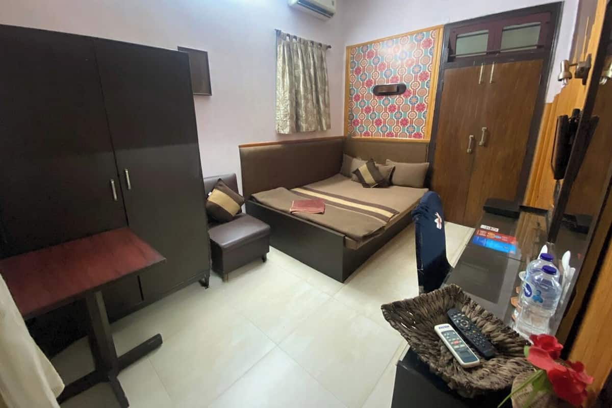 A compact room with a bed, a desk, a wardrobe, and a small table with a water bottle and remote control.