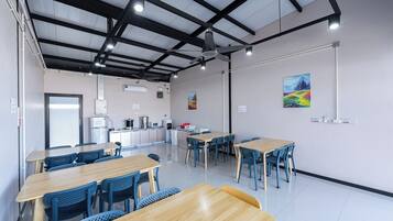 A modern dining area with wooden tables and blue chairs, a ceiling fan, and artwork on the walls.