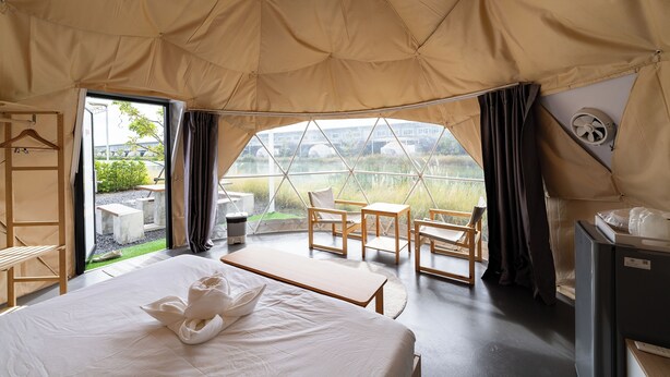 Een tent-achtige kamer met een bed, houten meubels en uitzicht op groen en gebouwen.