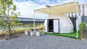Een koepelvormige tent met een deur, een picknicktafel en een klein tuinareaal met kunstgras.