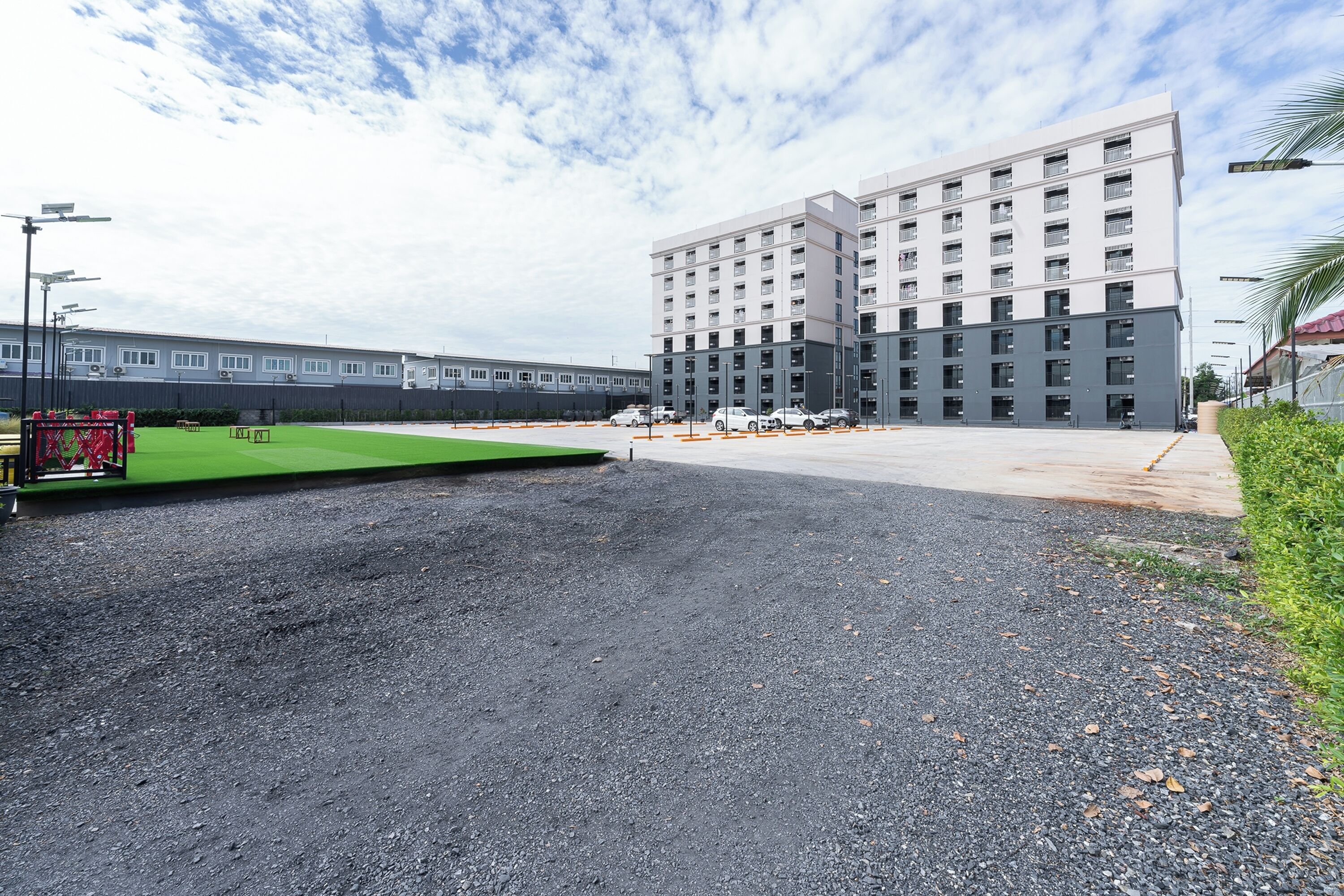 A modern building with multiple floors, a parking lot, and a green area.