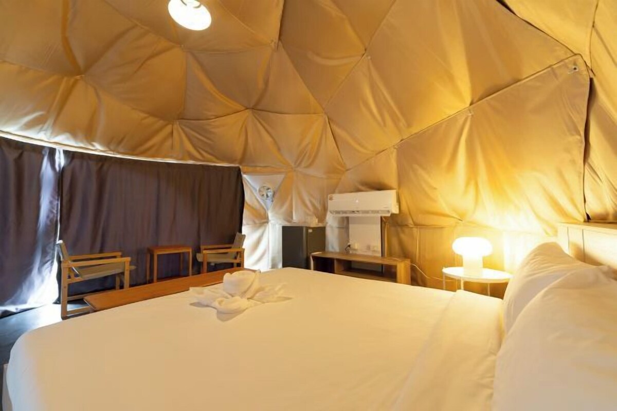 Una habitación acogedora con una cama grande, sillas de madera, una mesita y una lámpara.