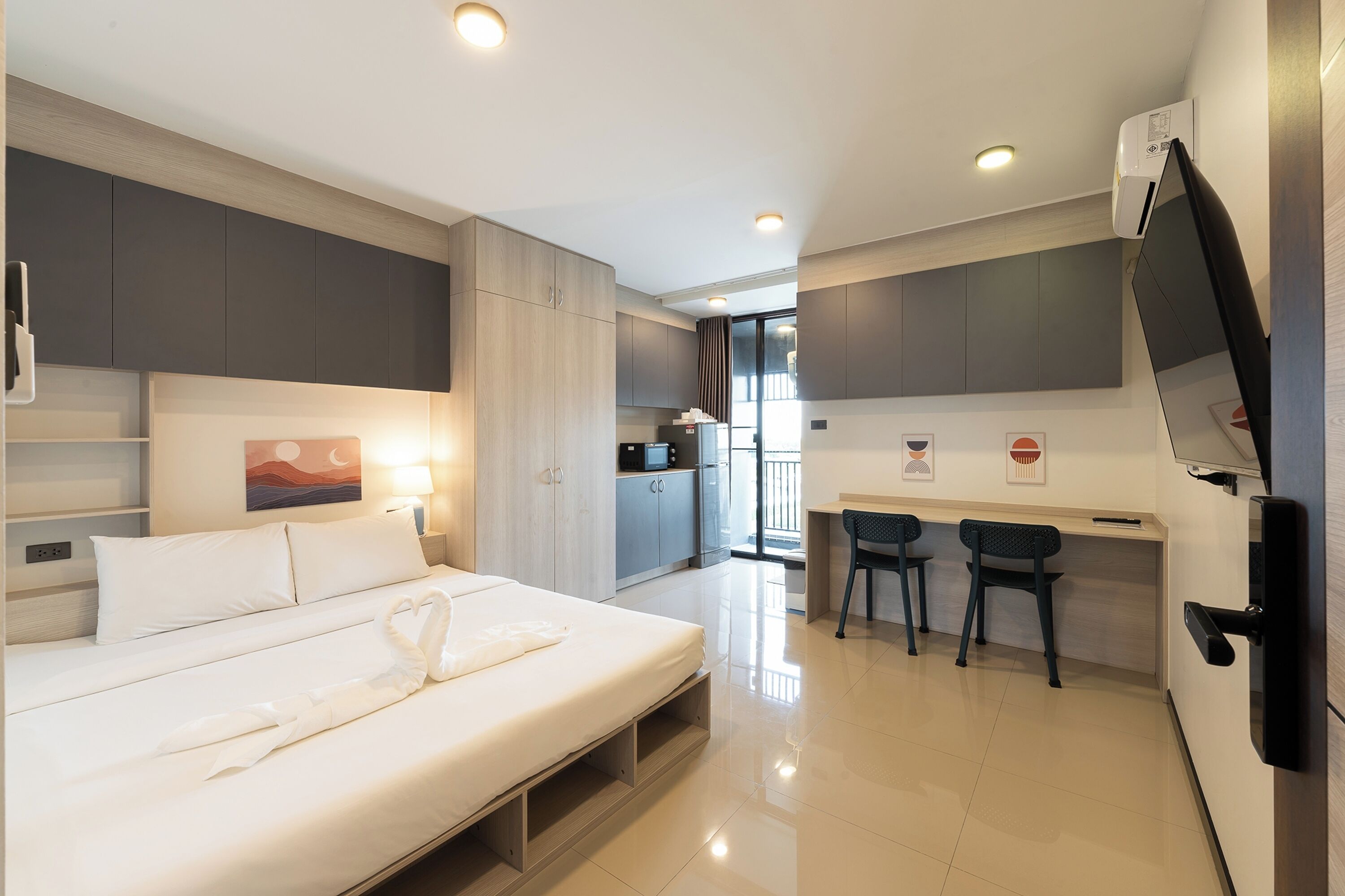 Una habitación de hotel moderna con una cama, un escritorio, dos sillas y un televisor.