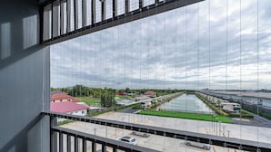 Uitzicht vanaf een balkon op een parkeerplaats, met een gracht en gebouwen op de achtergrond.