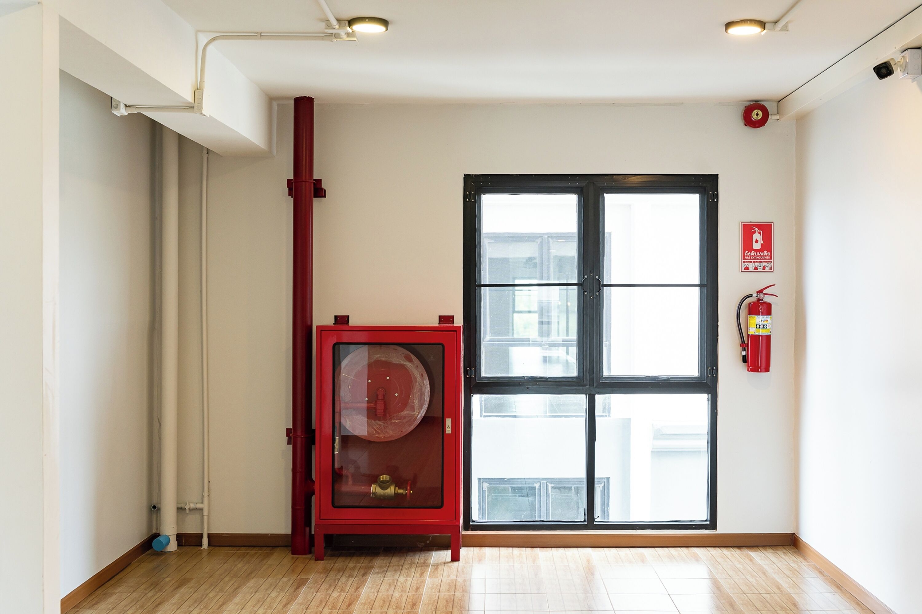 A room with a large window, a red fire extinguisher, and a fire alarm on the wall.
