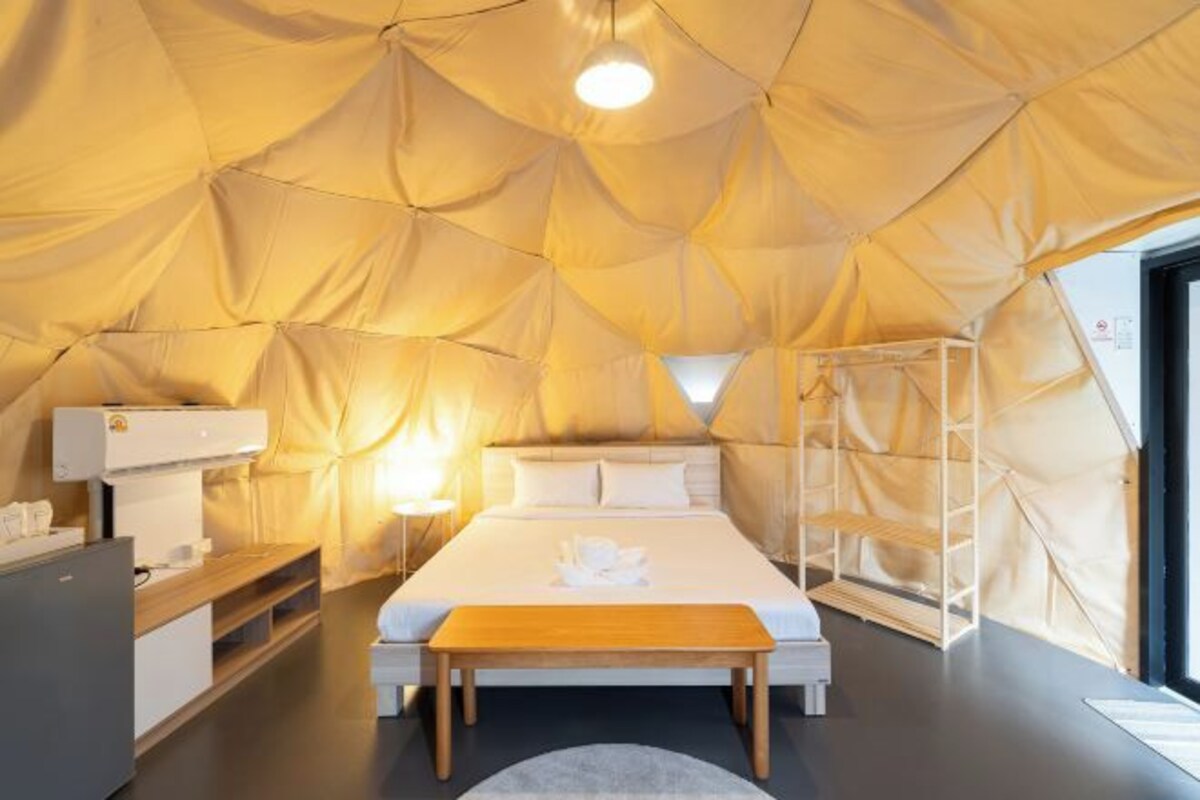Habitación tipo tienda con cama, mesita de noche y lámpara, además de una escalera.