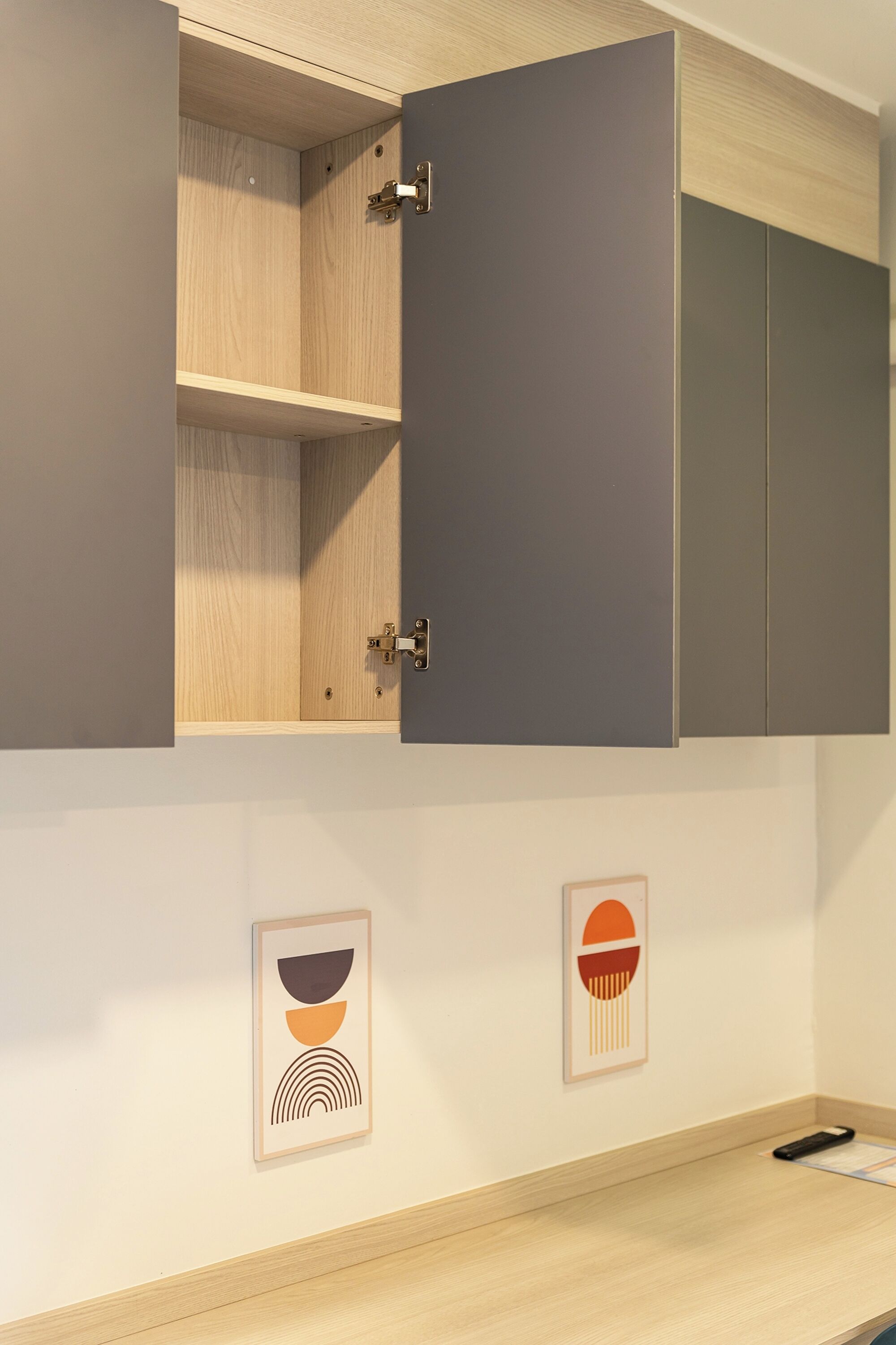 A room with a wooden cabinet, a grey door, and two framed abstract art pieces on the wall.