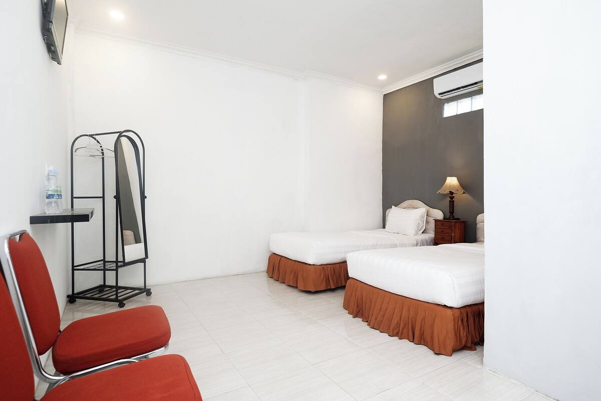Een hotelkamer met twee bedden, een stoel, een kleine tafel en een airconditioner bevestigd aan de muur.