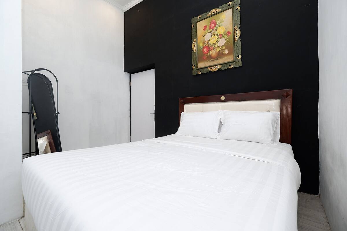 Een net opgemaakt bed met witte lakens in een kamer met zwarte wanden en een houten hoofdeinde.