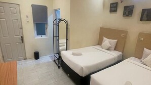Een hotelkamer met twee bedden, een houten bureau, een prullenbak en een raam.