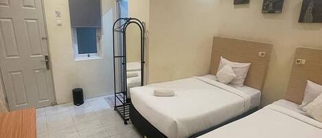 A hotel room with two beds, a wooden desk, a trash bin, and a window.
